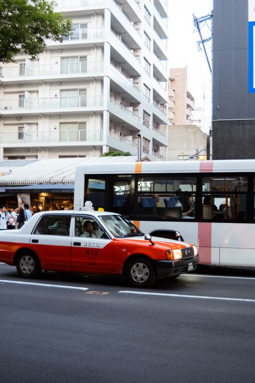 Free A busy street with a classic red and white taxi and a bus passing by, capturing urban life. Stock Photo
