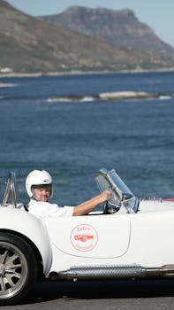 Classic Cobra car driven by a man along a scenic coastal road, reflecting vintage flair.