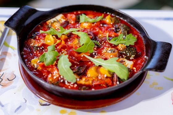 Chunky roasted vegetables in rich tomato sauce topped with arugula and sesame in a clay dish