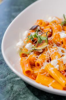A vibrant rigatoni pasta dish with figs and cheese in a rich tomato sauce, garnished beautifully.