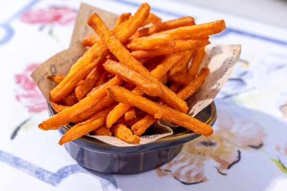 Thin orange sweet potato fries piled in a paper-lined dark ceramic bowl on a floral tablecloth