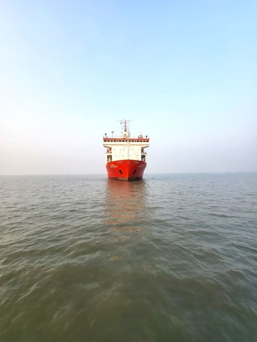 Free A red cargo ship navigating a calm sea under a clear sky during dusk. Stock Photo