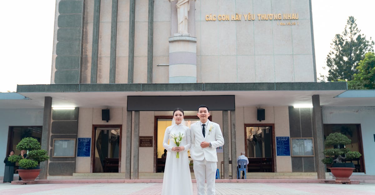 Bride and groom in white attire pose outside a church with peaceful ambiance.