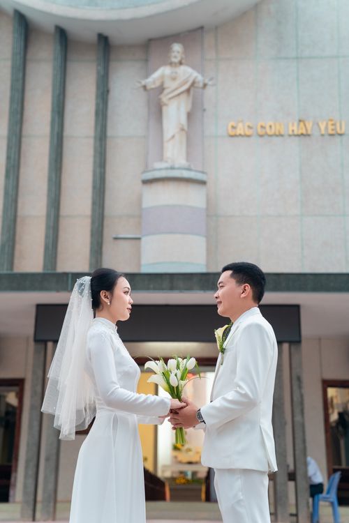 Free A bride and groom stand in front of a church holding flowers. Stock Photo