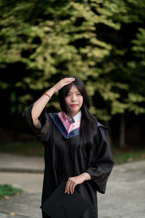 Free A young woman in a graduation gown holding a cap outdoors, celebrating her achievement. Stock Photo