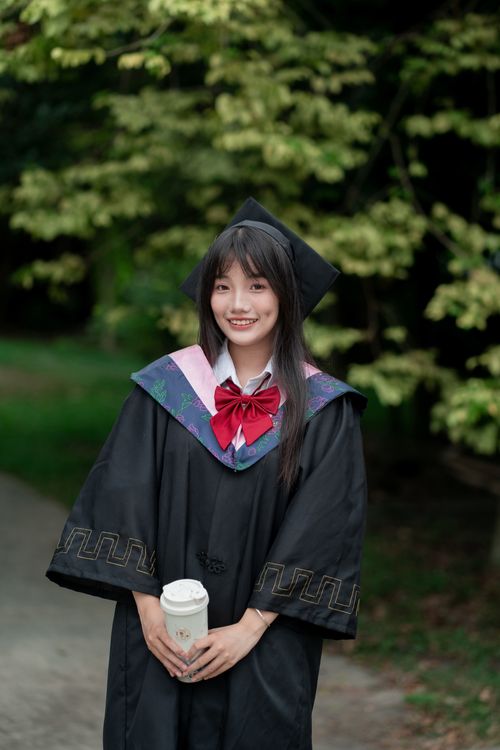 Free A young woman in graduation attire holds a coffee cup outdoors, smiling confidently. Stock Photo