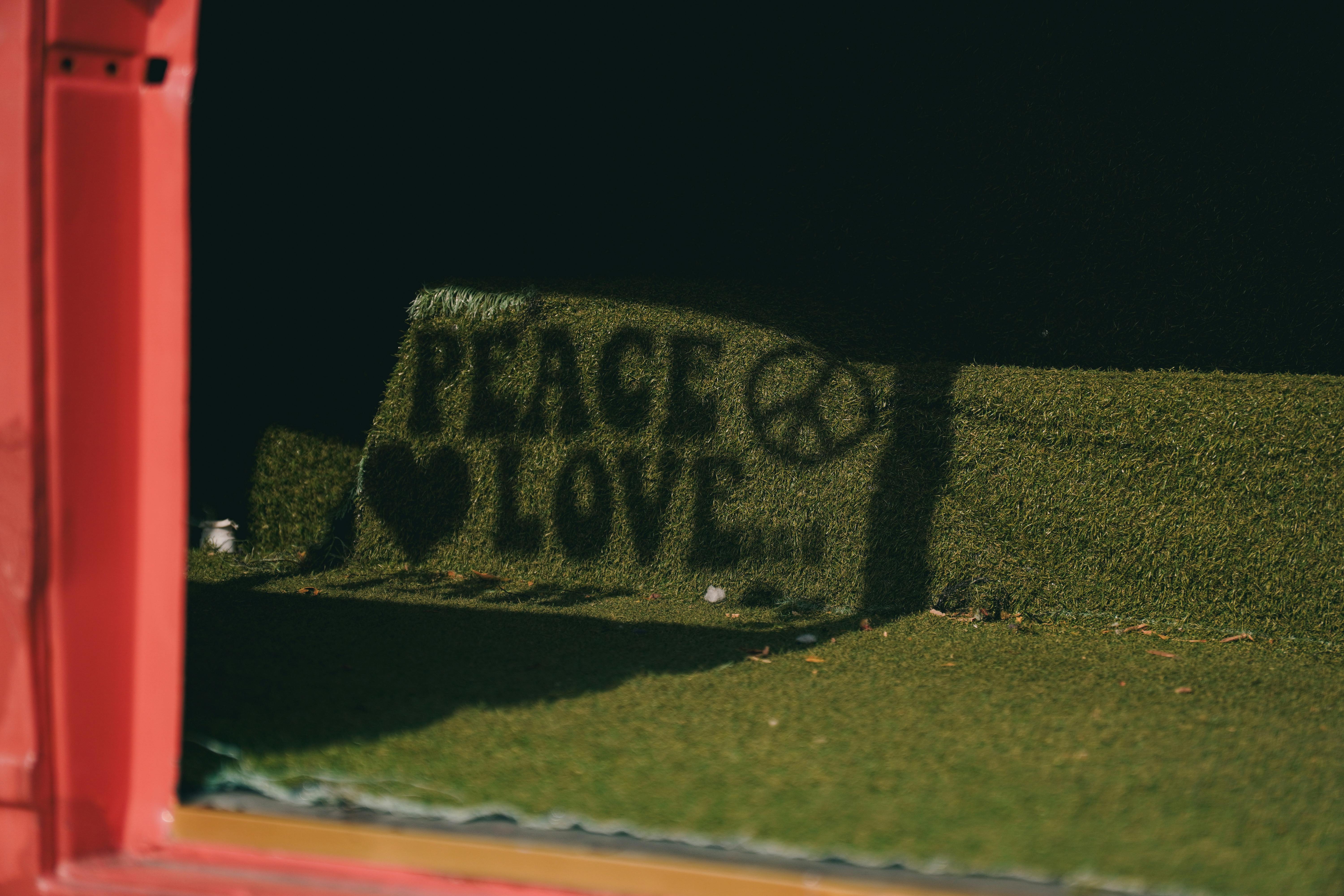 Gratis Sombra creativa del cartel "Paz y Amor" con el símbolo de la paz sobre césped artificial. Foto de stock