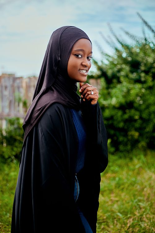 Free Portrait of a young woman wearing a hijab, smiling in an outdoor setting with greenery. Stock Photo