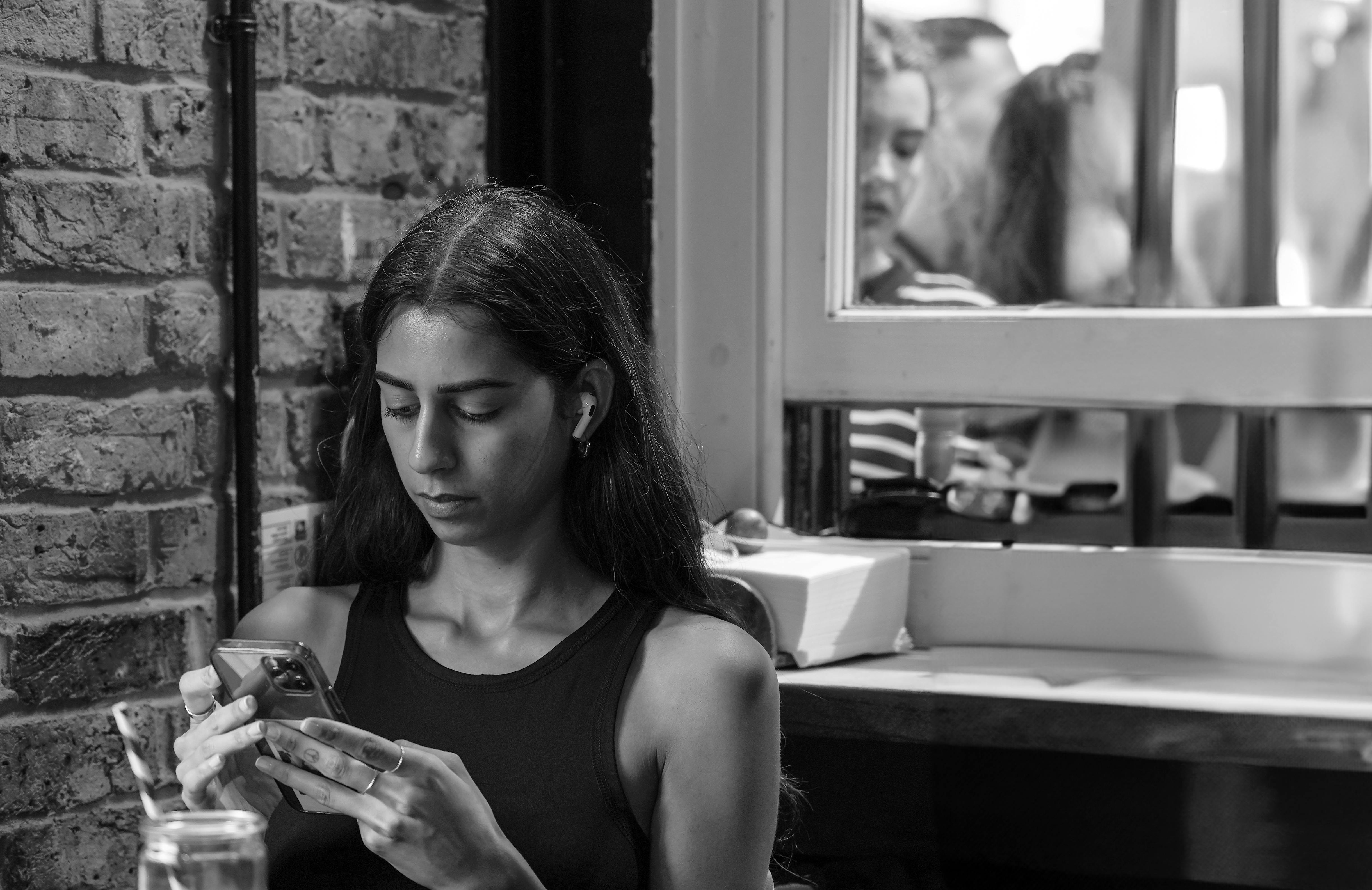 wireless earbuds with long battery life uk - A young woman focused on her smartphone indoors, expressing modern lifestyle.