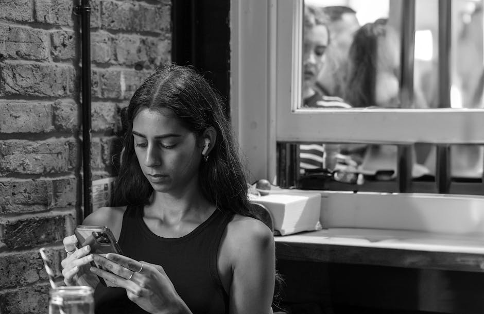 wireless earbuds with long battery life uk - A young woman focused on her smartphone indoors, expressing modern lifestyle.
