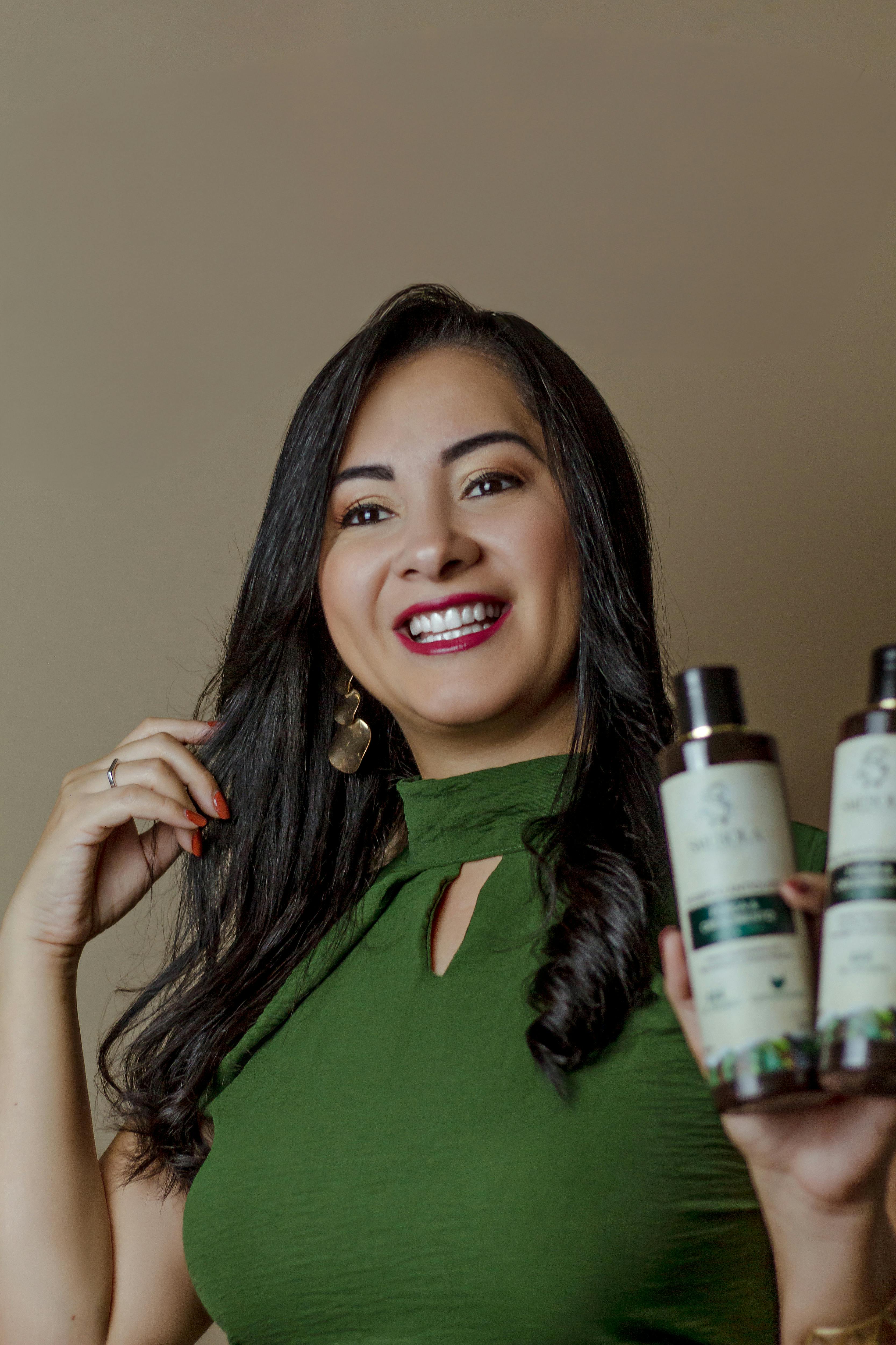 Woman in green top smiling and holding bottles of hair care products, promoting beauty and wellness.