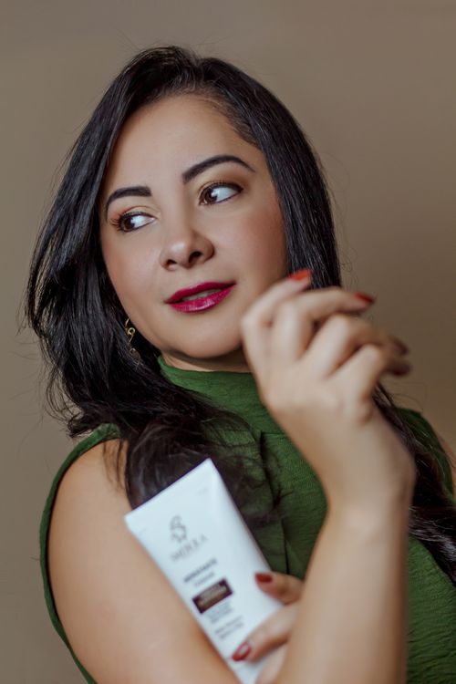 Free Fashionable woman with dark hair holding a skincare bottle, exuding elegance and style. Stock Photo