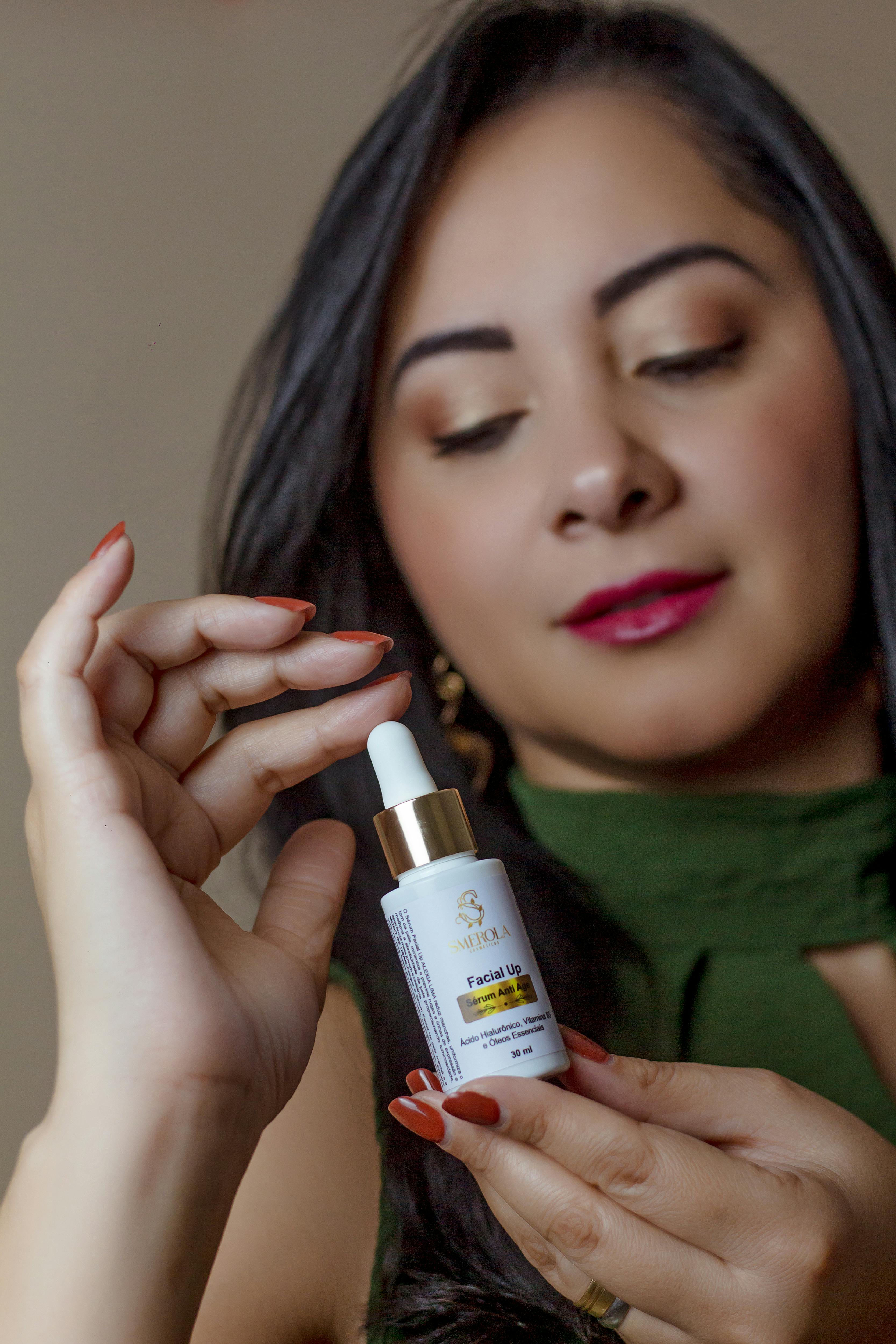 A woman displays a bottle of facial oil with a dropper, promoting skincare indoors.