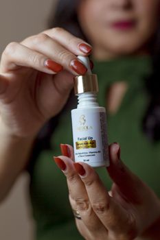 A close-up shot of a woman in green holding a facial serum bottle with manicured nails.
