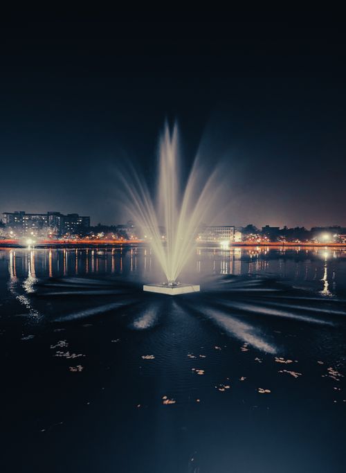 Free A stunning illuminated fountain in a cityscape at night, showcasing vibrant lights and reflections. Stock Photo