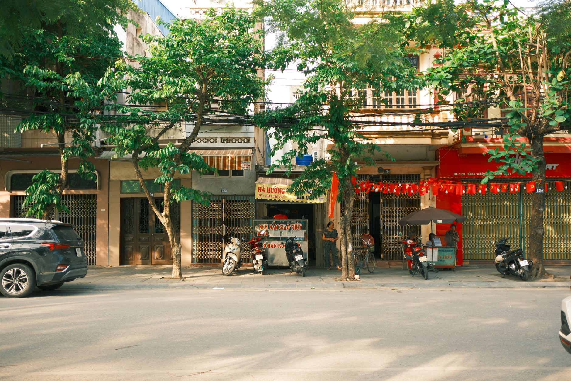 Sunny street scene in Nam Định, Vietnam with parked motorbikes and storefronts.