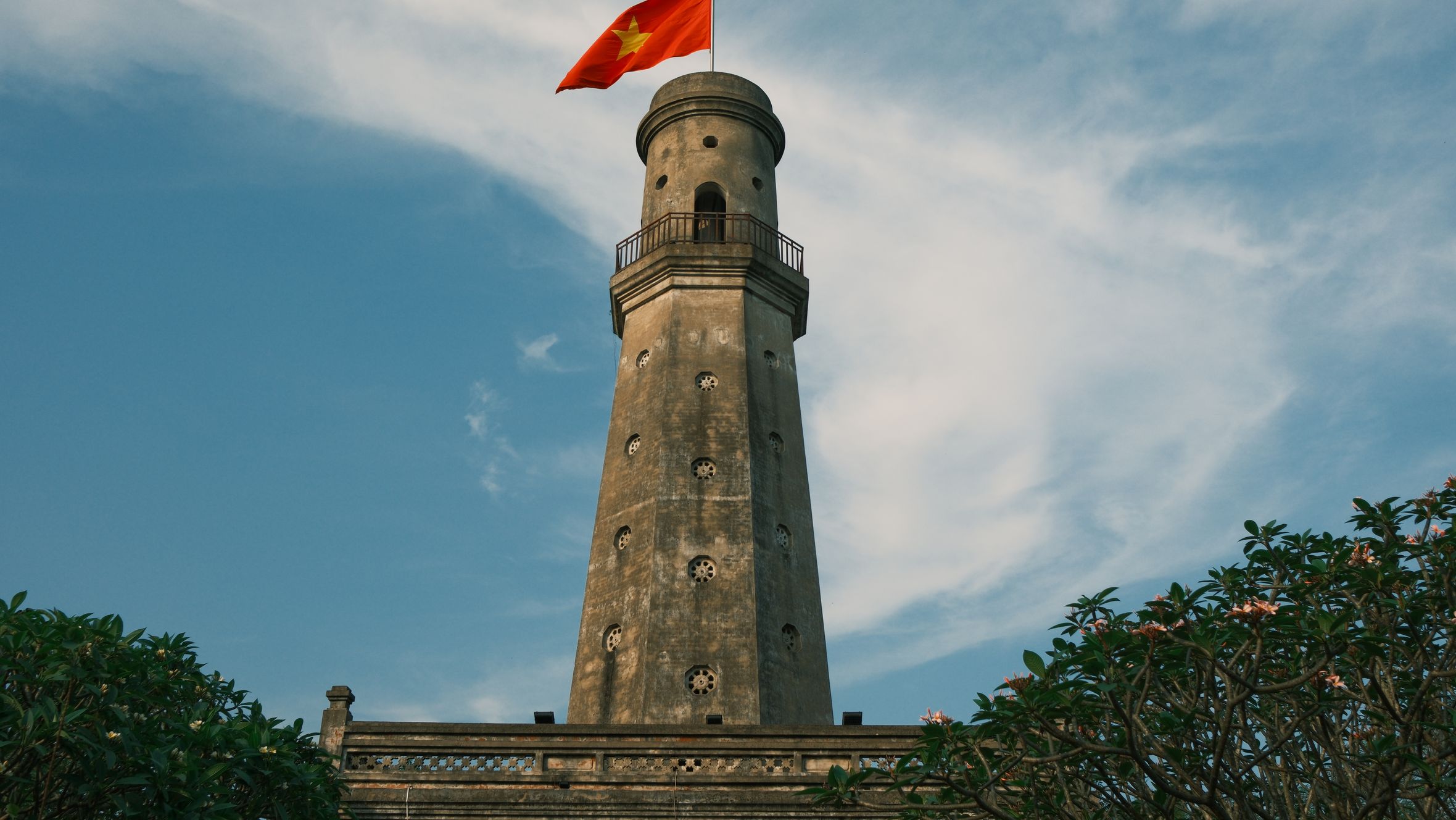 A scenic view of a historic lighthouse in Nam Định, Vietnam, crowned with the Vietnamese flag.