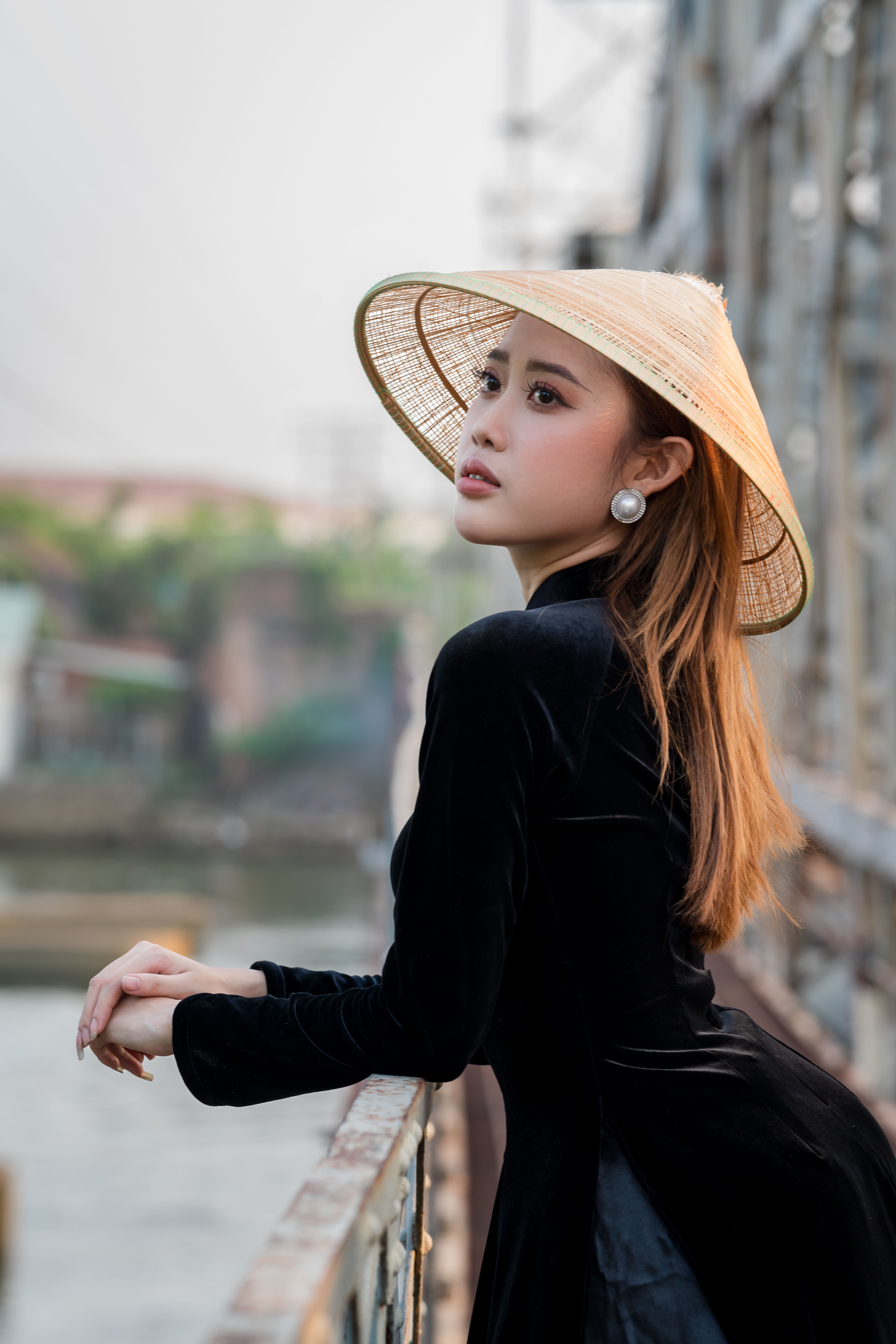Elegant woman in traditional outfit with a conical hat on a bridge, embodying cultural grace.