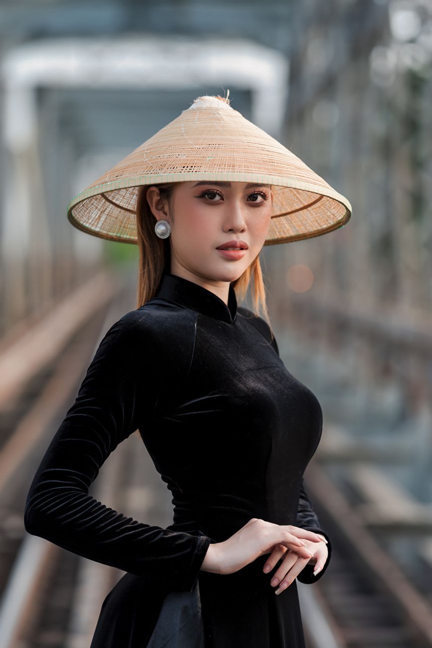 Woman in a conical hat poses elegantly on a bridge, showcasing cultural attire with a modern twist.