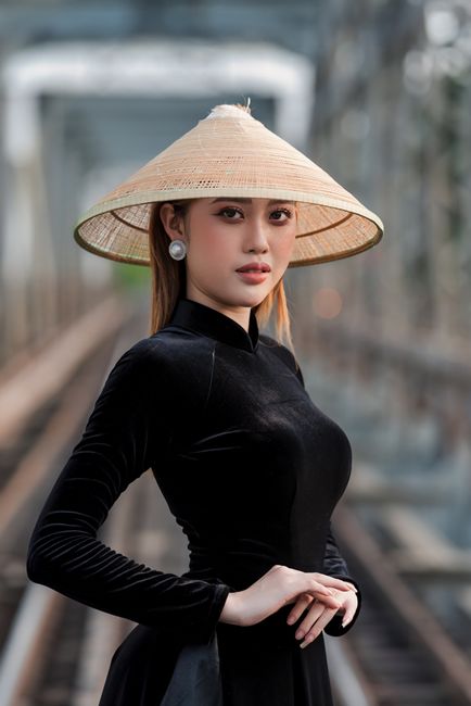 Woman in a conical hat poses elegantly on a bridge, showcasing cultural attire with a modern twist.