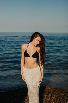 Elegant woman in beachwear standing by the ocean under clear blue sky.