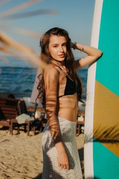 A woman in swimwear posing stylishly on a sunny beach with a surfboard, embracing summer vibes.