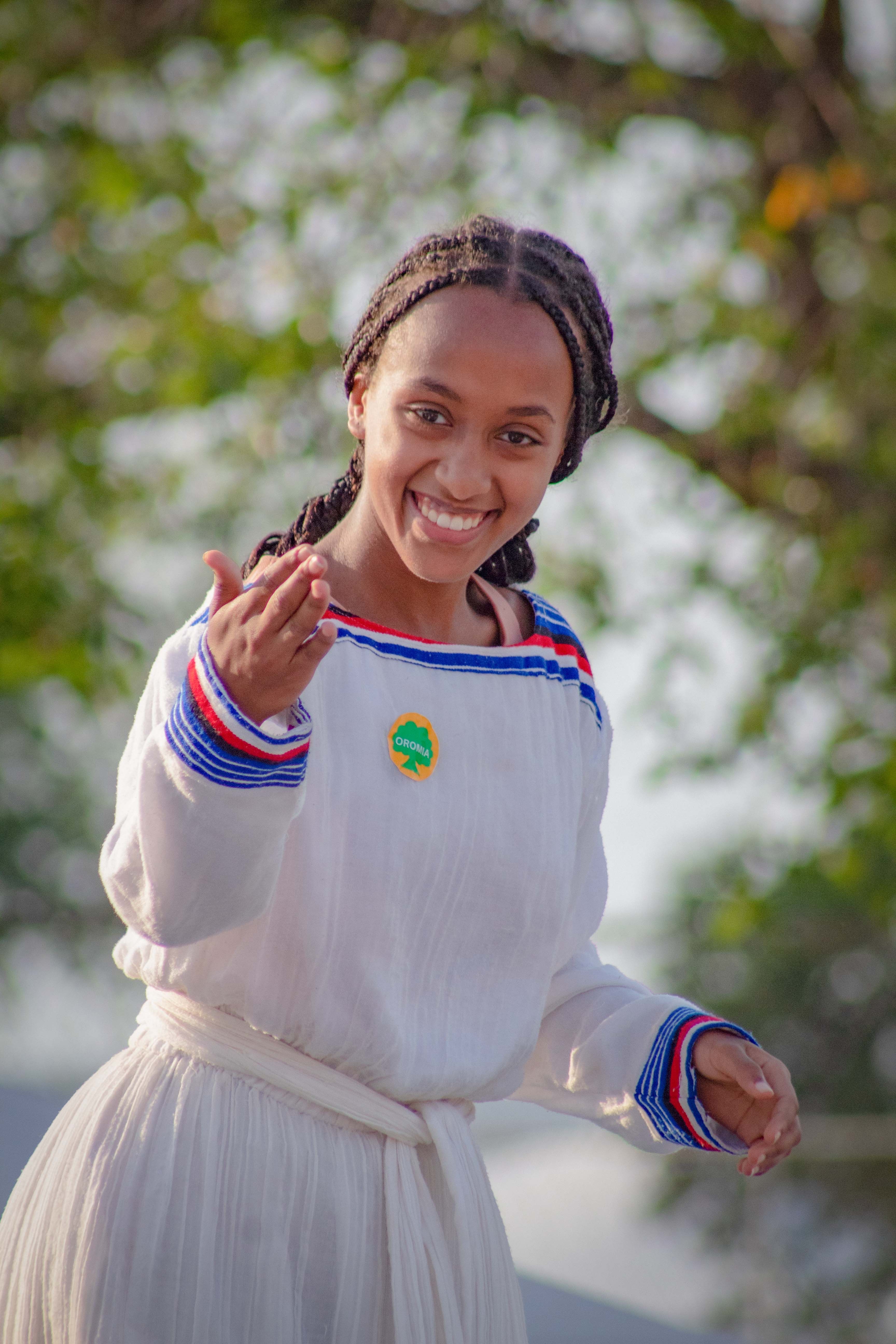 A joyful woman wearing traditional Ethiopian attire smiles outdoors in a natural setting.