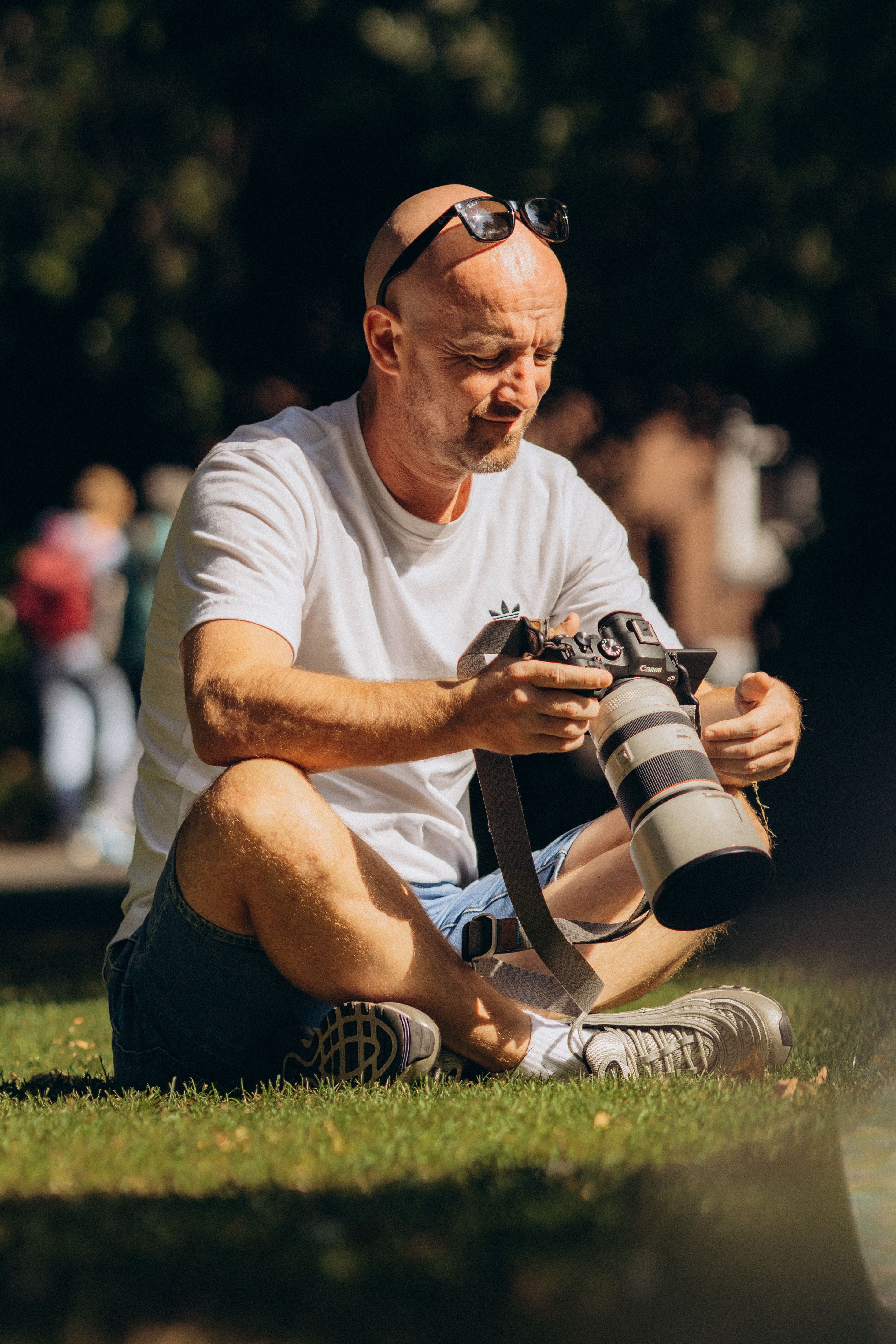 Casual moment of a male photographer adjusting his camera outdoors in a sunlit park.