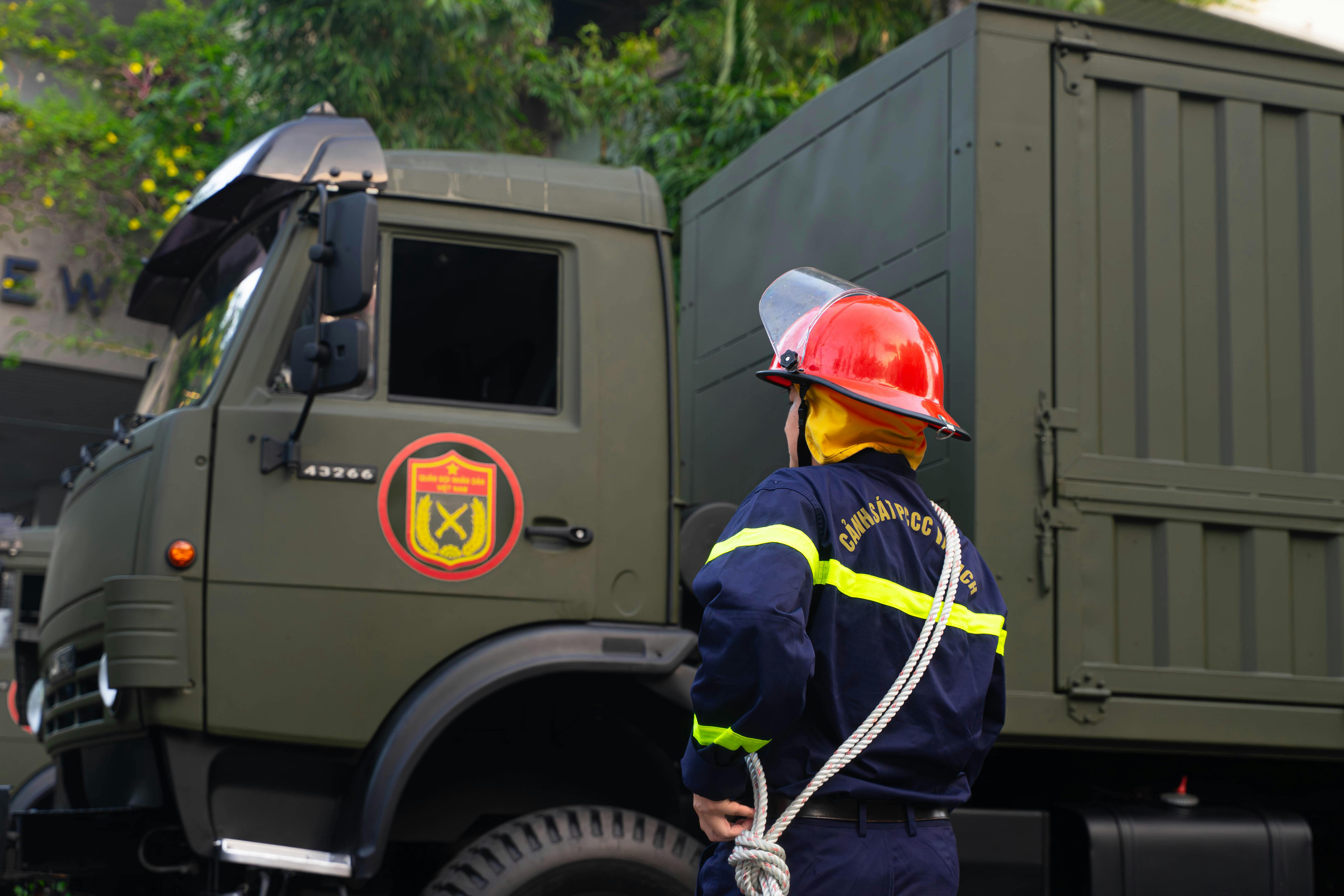 Firefighter in uniform with protective gear stands by an army truck outdoors.