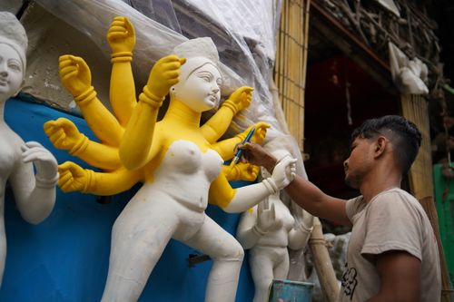 Free An artist meticulously paints a Hindu goddess idol in a vibrant workshop setting, showcasing cultural craftsmanship. Stock Photo
