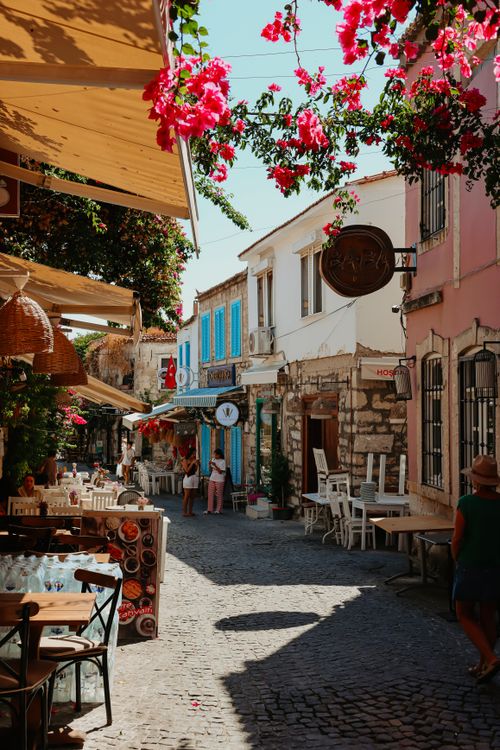 Free Quaint cobblestone street with cafes, vibrant flowers, and historic Mediterranean architecture. Stock Photo