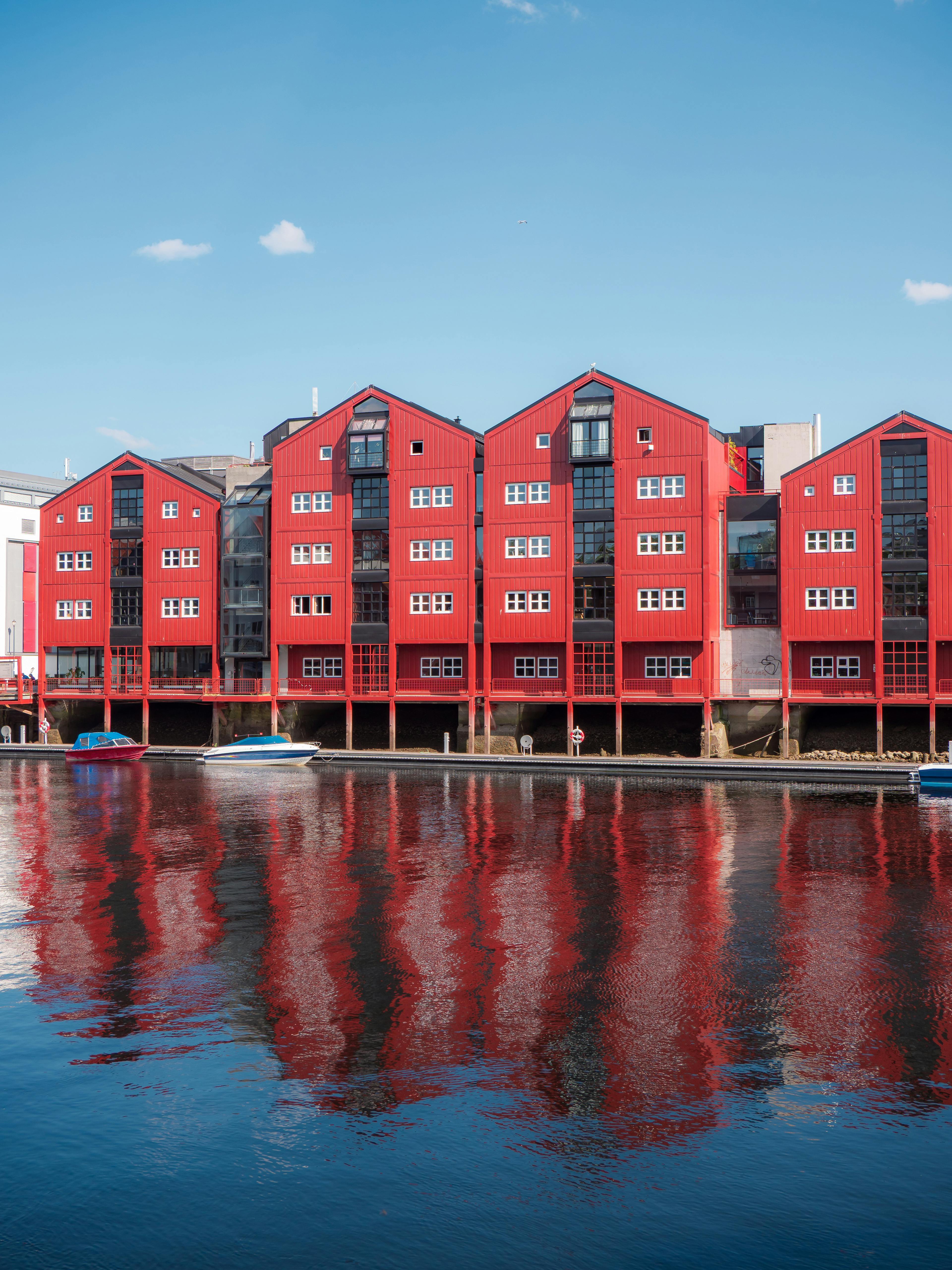Colorful red houses reflecting in calm water under a clear sky. Scenic Nordic architecture.