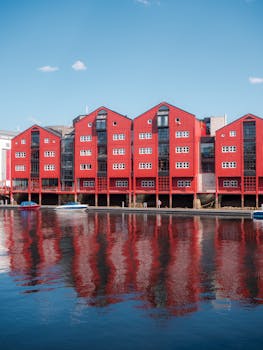 Colorful red houses reflecting in calm water under a clear sky. Scenic Nordic architecture.
