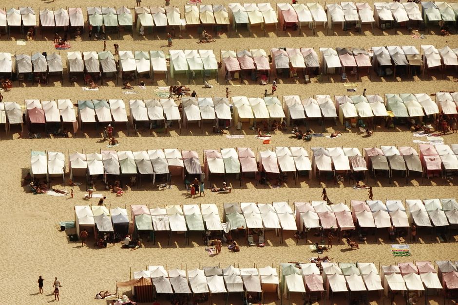 Aerial view of rows of colorful beach tents on a sunny sandy beach with people relaxing.