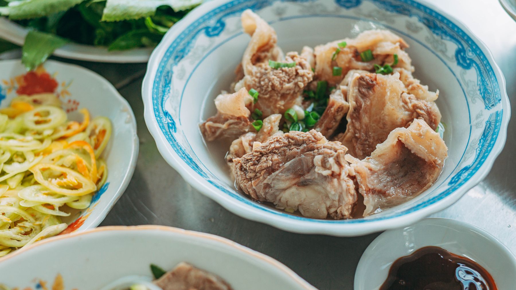 A vibrant bowl of Vietnamese beef noodles garnished with herbs, served with fresh vegetables.