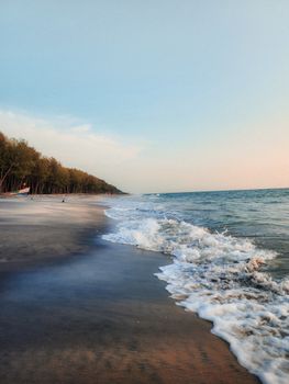 A tranquil beach scene at sunset with gentle waves and a distant forest line.