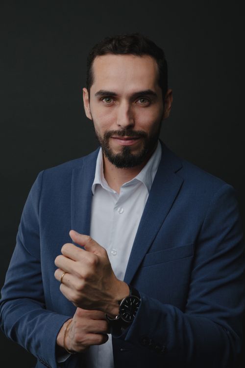 Free Portrait of a confident businessman in a blue suit adjusting his watch with a professional demeanor. Stock Photo