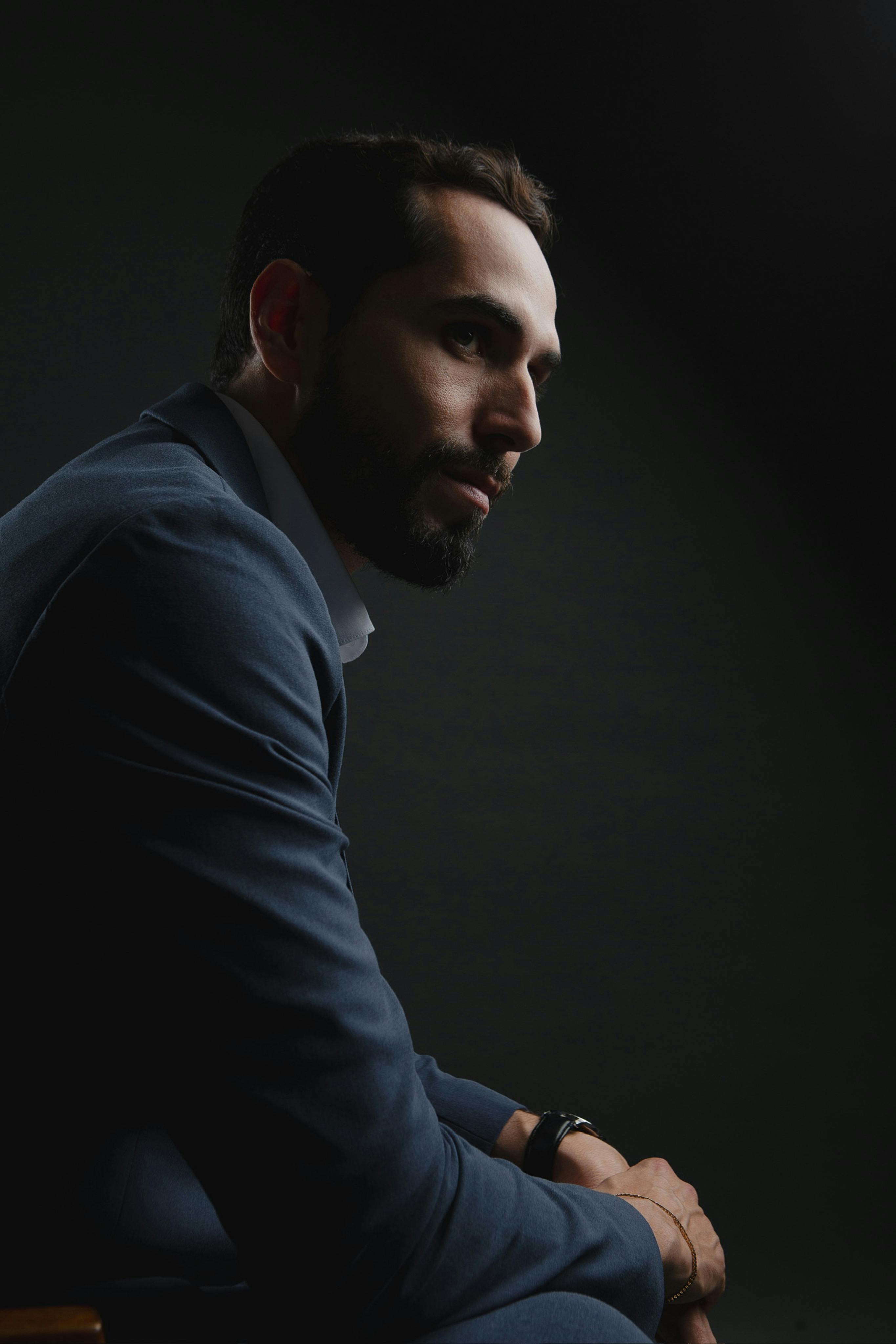 Dramatic portrait of a man in a dark suit with moody lighting.