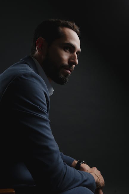 Dramatic portrait of a man in a dark suit with moody lighting.