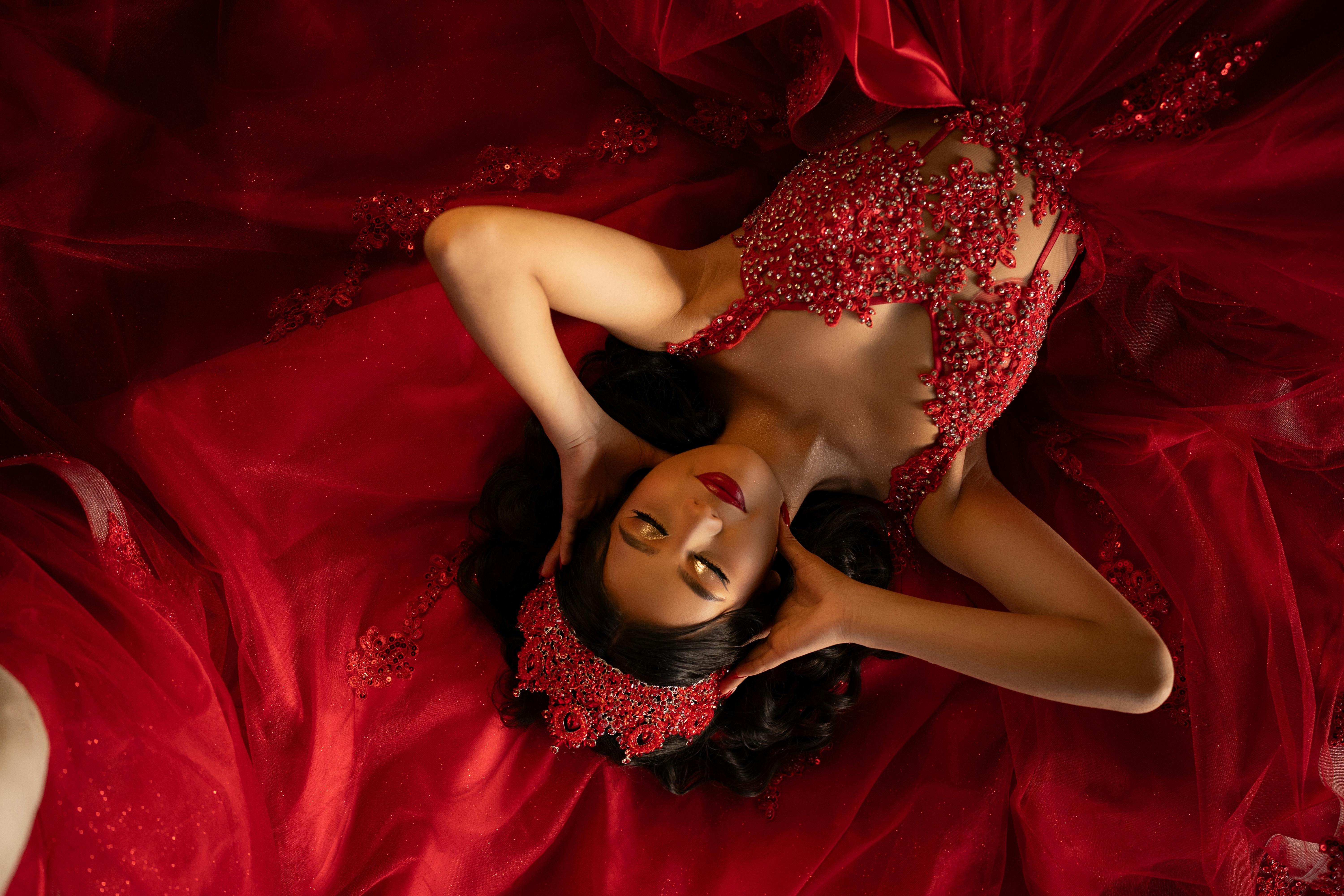 A stunning woman in a red beaded gown lies gracefully, showcasing elegance.