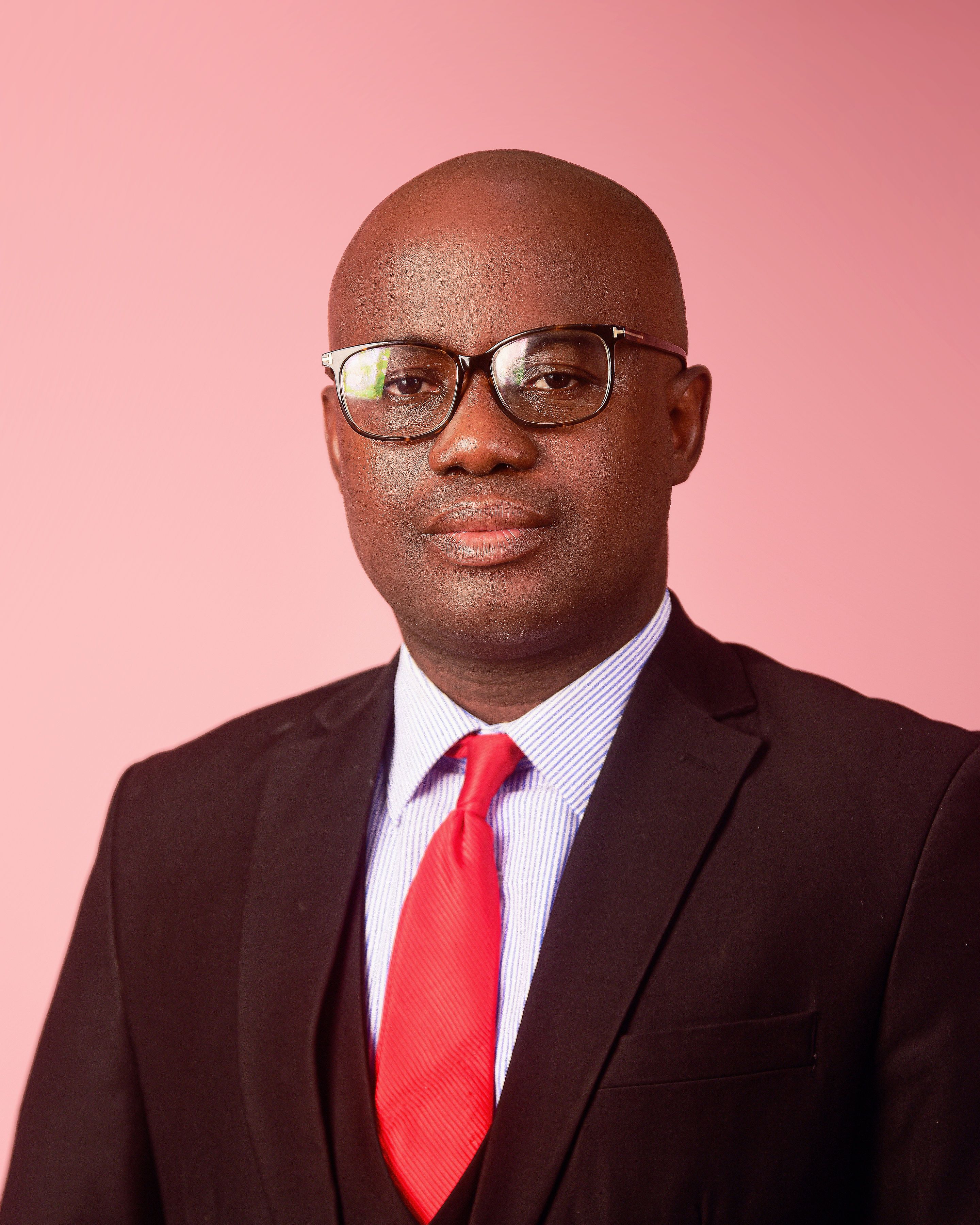 Professional portrait of an adult man in suit with red tie on pink background.