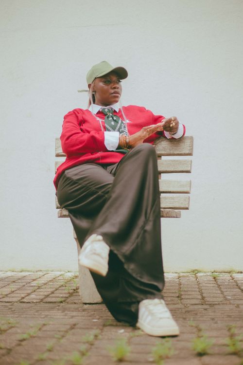 Free Chic urban fashion featuring red sweater, loose pants, and casual cap on a bench. Stock Photo