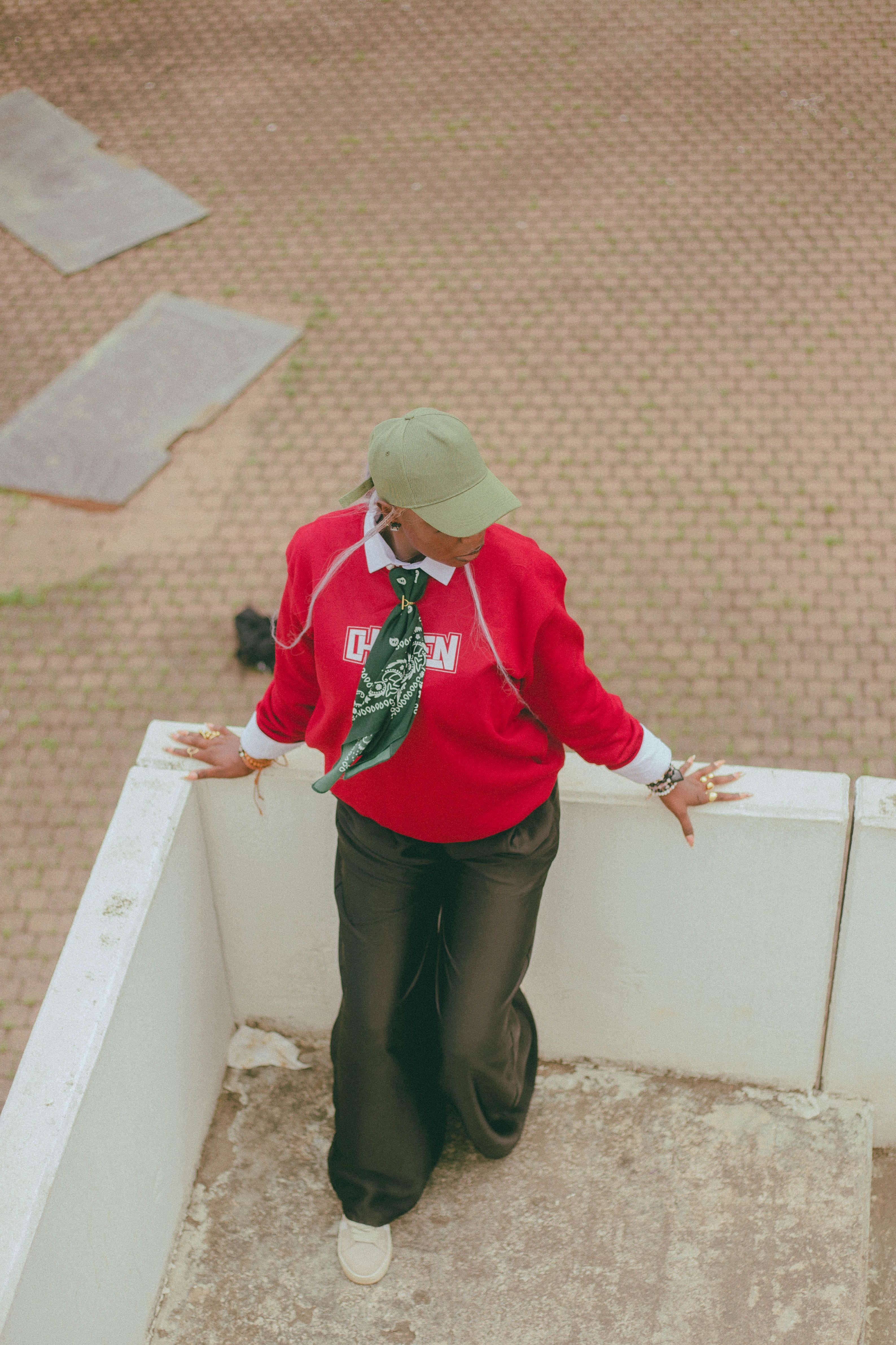 Person in stylish red sweatshirt and cap poses outdoors in a modern, urban setting.