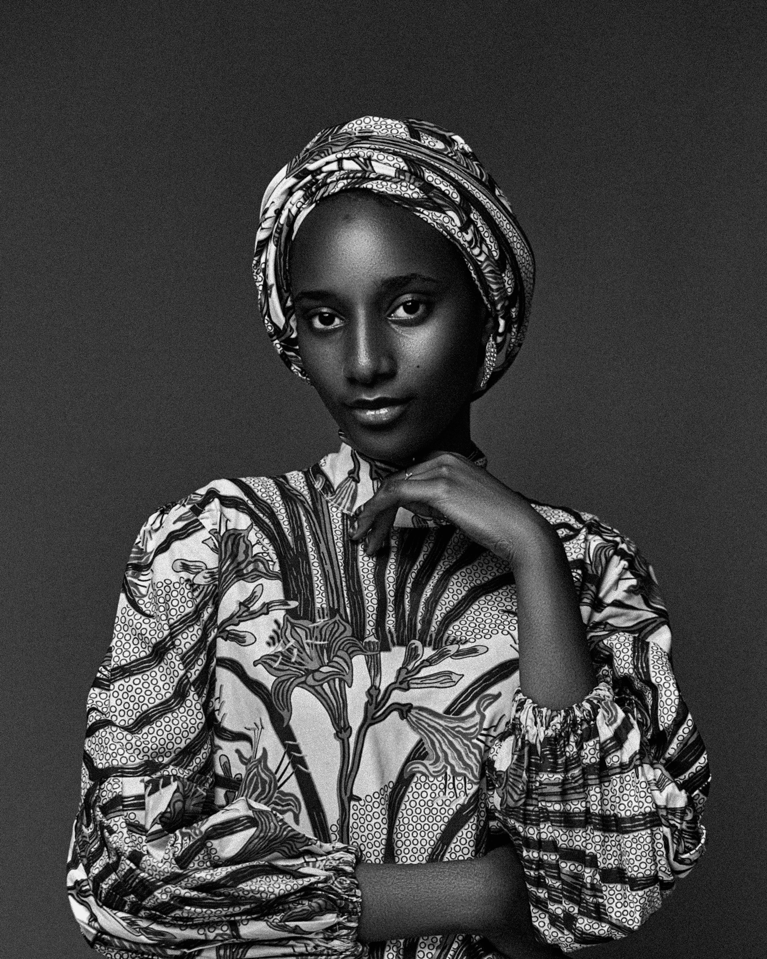Striking black and white portrait of a woman in traditional Nigerian dress and headscarf, exuding grace and confidence.