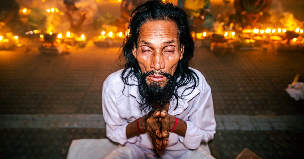 A man meditates with closed eyes surrounded by lit candles in an outdoor ritual.