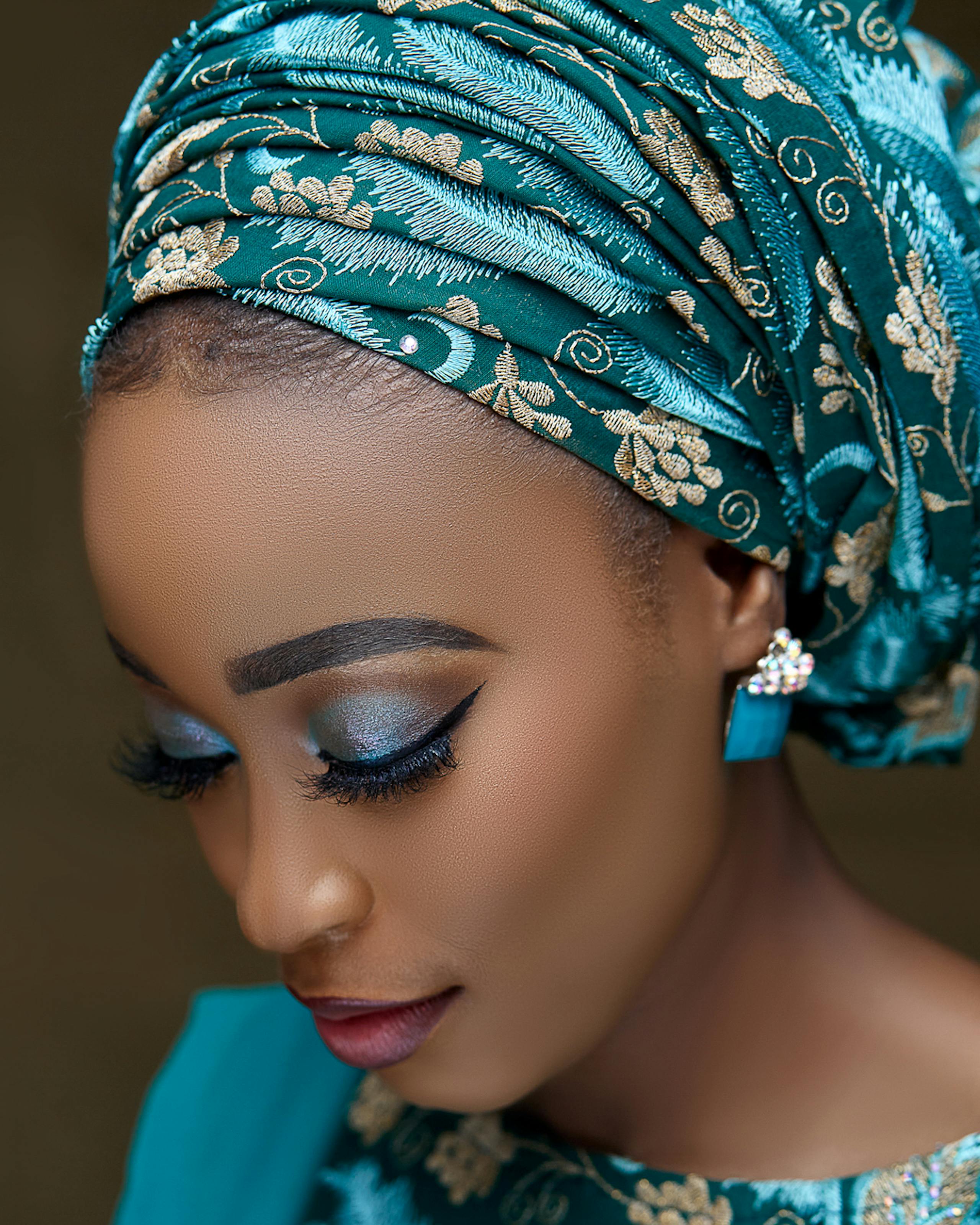 Free Close-up portrait of a Nigerian woman wearing traditional teal and gold attire, showcasing elegance and beauty. Stock Photo