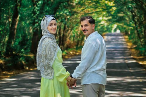 Free A couple holding hands and smiling on a peaceful, tree-lined road in the daytime. Stock Photo