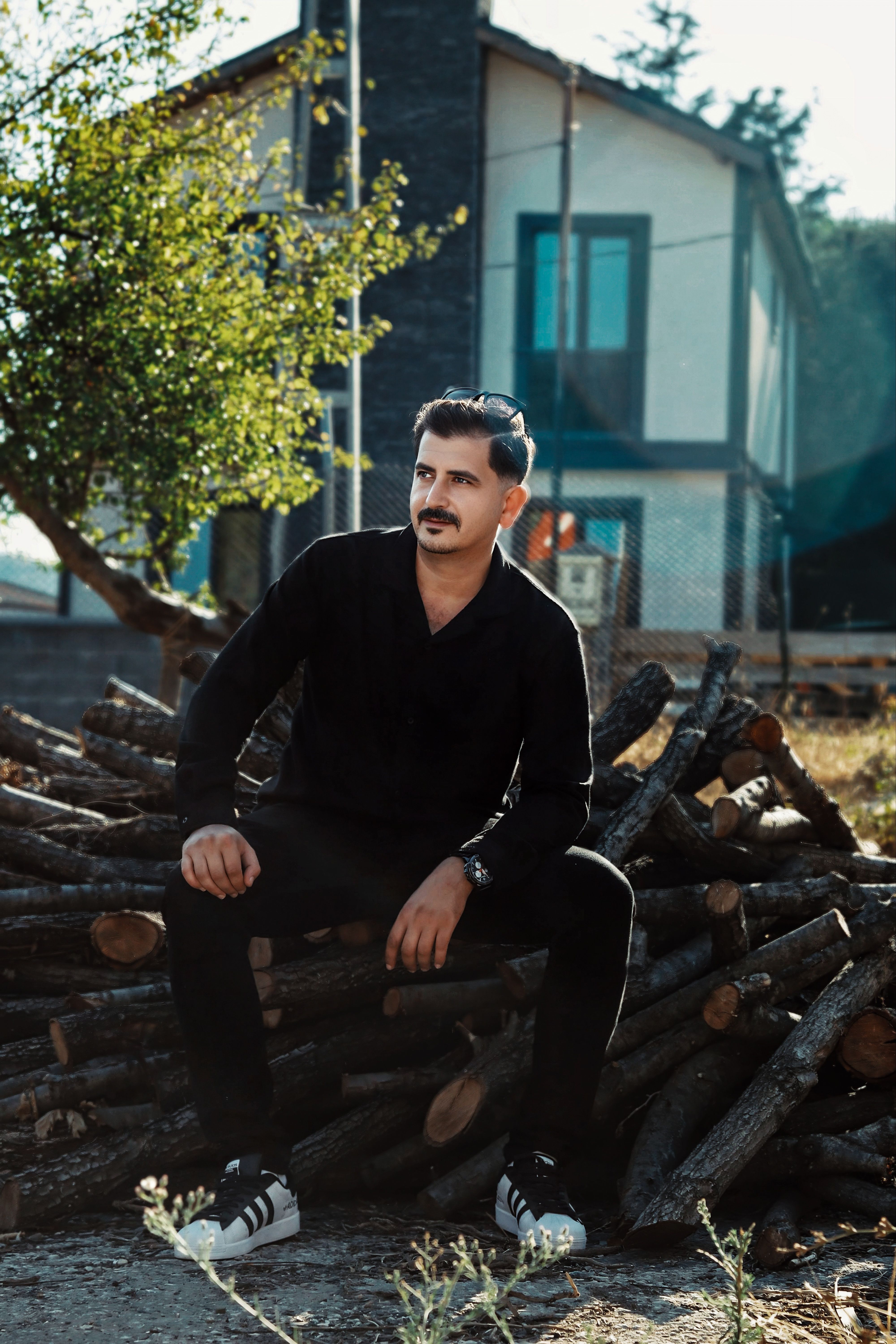 Young man relaxing on a stack of logs outdoors in front of a modern house.