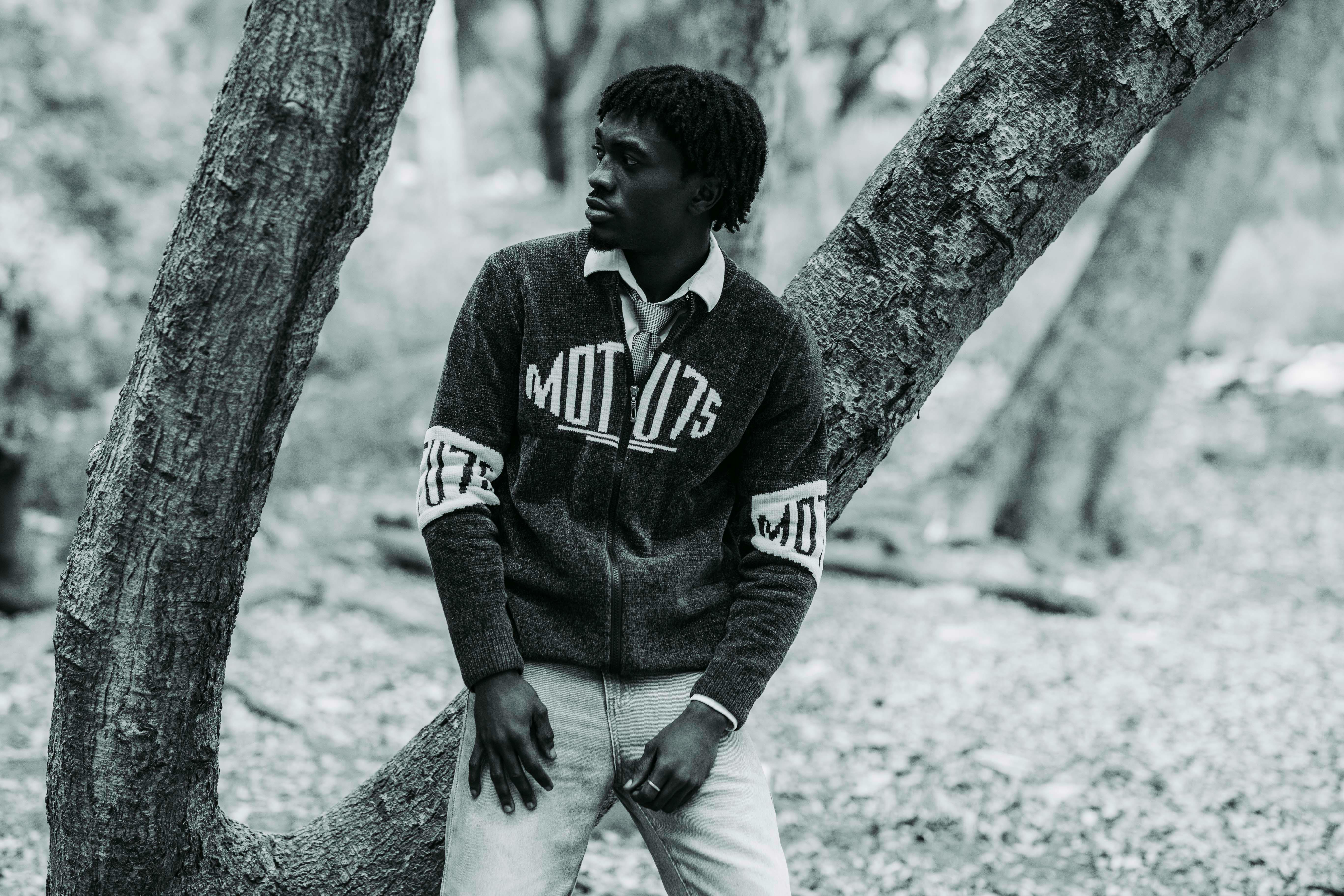 Stylish black and white portrait of a man leaning against a tree outdoors.