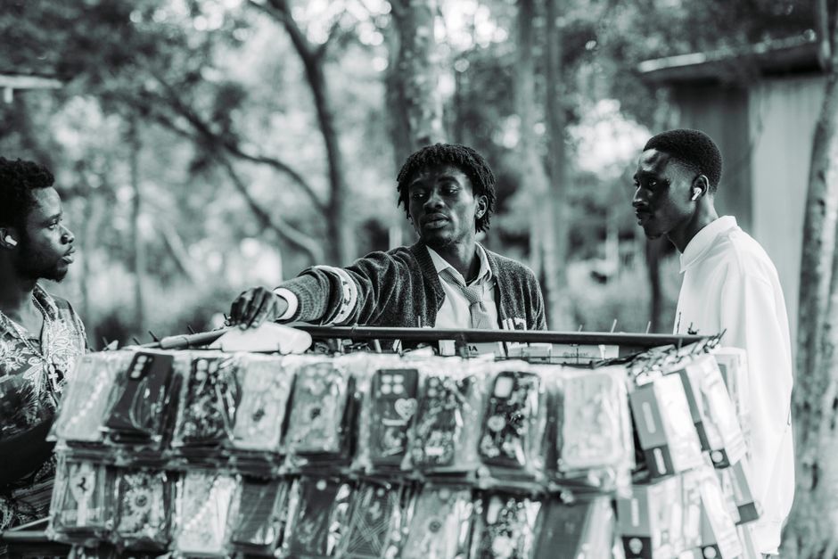 Candid black and white photo capturing a street vendor selling mobile accessories in Accra, Ghana.